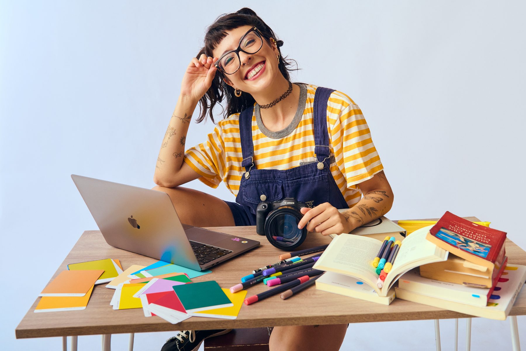 Magui Medina sonriendo en su escritorio de trabajo con cámara, laptop, libros y paletas de color